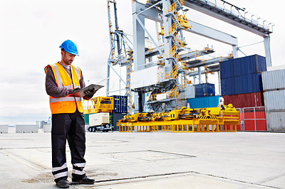 Buy stock photo Shot of a young man in workwear using a digital tablet while standing on a large commercial dock