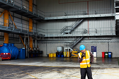 Buy stock photo Shot of a young man in workwear talking on a walkietalkie while standing on a large commercial dock