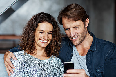 Buy stock photo Shot of a happy couple sitting on their sofa reading a text message