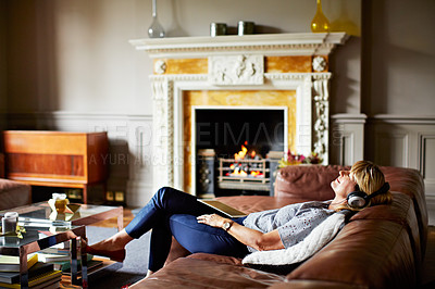Buy stock photo Shot of a mature woman lying back on her sofa listening to music on a digital tablet