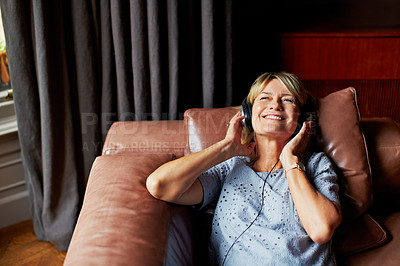 Buy stock photo Shot of a mature woman lying back on her sofa listening to music on headphones