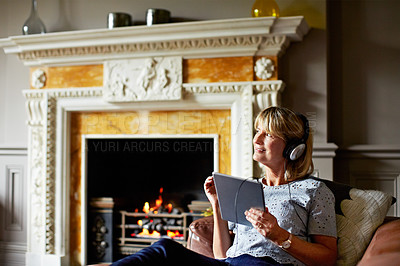 Buy stock photo Shot of a mature woman lying back on her sofa listening to music on headphones