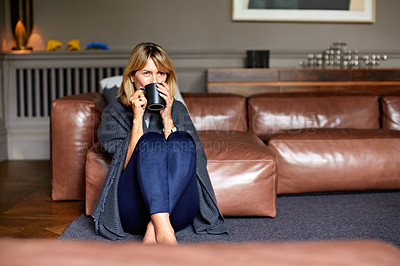 Buy stock photo Shot of a mature woman sitting on her living room floor drinking tea while wrapped in a blanket