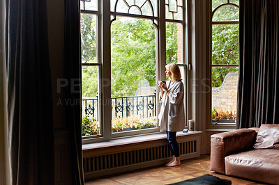 Buy stock photo Shot of a mature woman drinking tea while looking out of her living room window