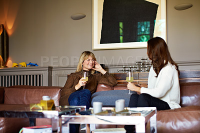 Buy stock photo Shot of two women sitting on a sofa drinking wine and talking