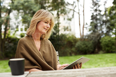 Buy stock photo Shot of a mature woman sitting in her yard drinking tea and using a digital tablet