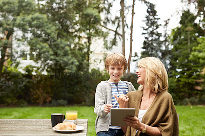 Buy stock photo Shot of a grandmother and her grandson sitting at a table in her yard using a digital tablet