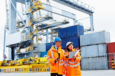 Buy stock photo Shot of two dock workers looking through paperwork while standing in a dockyard