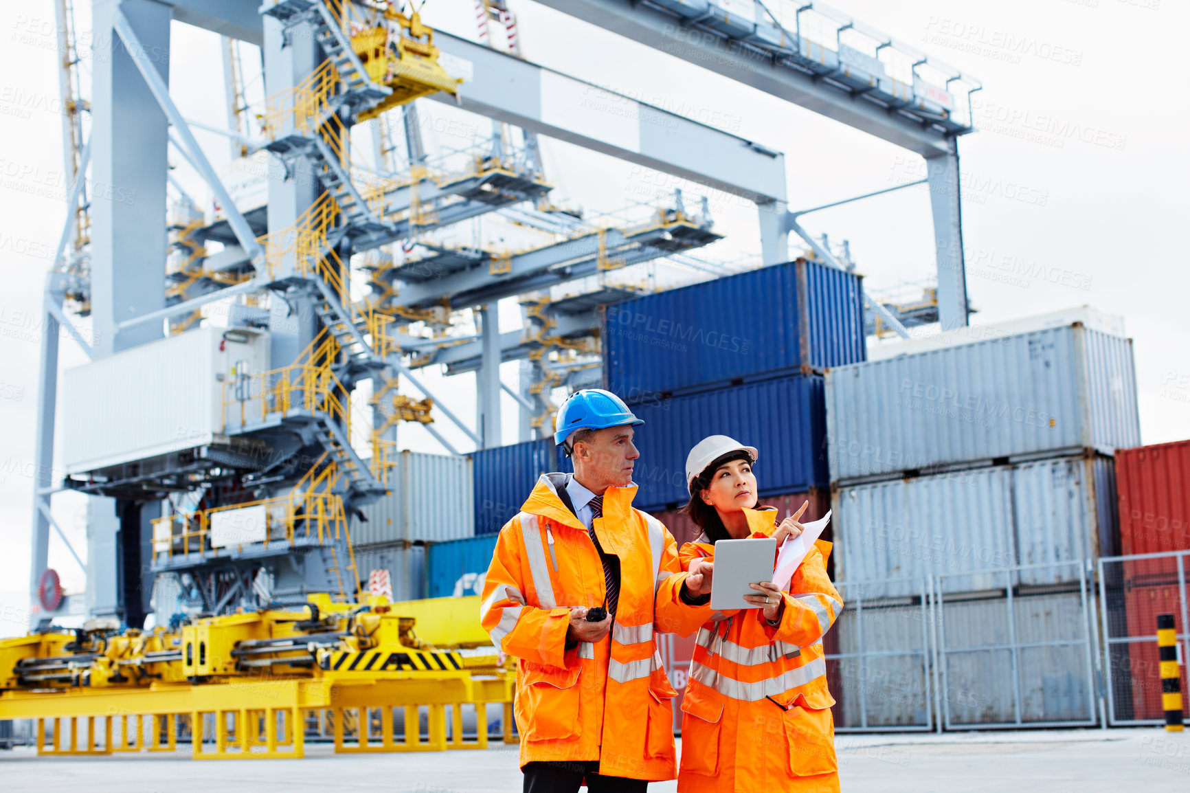 Buy stock photo Shot of two dock workers looking through paperwork while standing in a dockyard