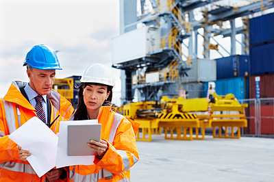 Buy stock photo Shot of two dock workers looking through paperwork while standing in a dockyard