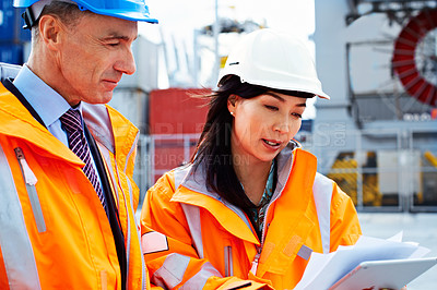 Buy stock photo Shot of two dock workers looking through paperwork while standing in a dockyard