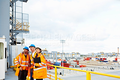 Buy stock photo Shot of three workers talking together while standing on a overhead walkway at a commercial dock