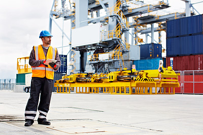 Buy stock photo Shot of a young man in workwear using a digital tablet while standing on a large commercial dock