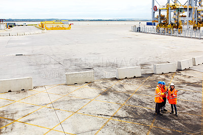 Buy stock photo High angle shot of three workers talking together while standing on a commercial dock