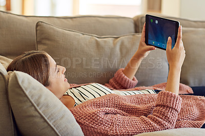 Buy stock photo Shot of a young woman lying on her sofa using a digital tablet