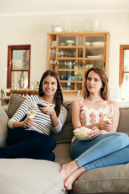 Buy stock photo Shot of two friends drinking wine and eating popcorn while watching a movie together on the sofa at home