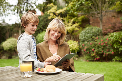 Buy stock photo Shot of a grandmother and her grandson sitting at a table in her yard using a digital tablet