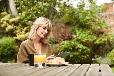 Buy stock photo Shot of a mature woman sitting in her yard having breakfast and using a digital tablet