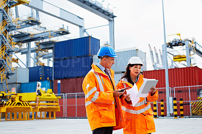 Buy stock photo Shot of two dock workers looking through paperwork while standing in a dockyard
