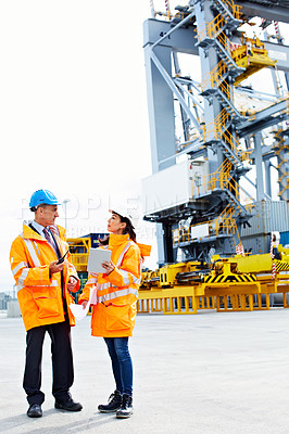 Buy stock photo Shot of two dock workers looking through paperwork while standing in a dockyard