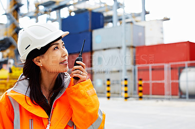 Buy stock photo Shot of a woman in workwear talking on a walkie talkie while standing on a commercial dock