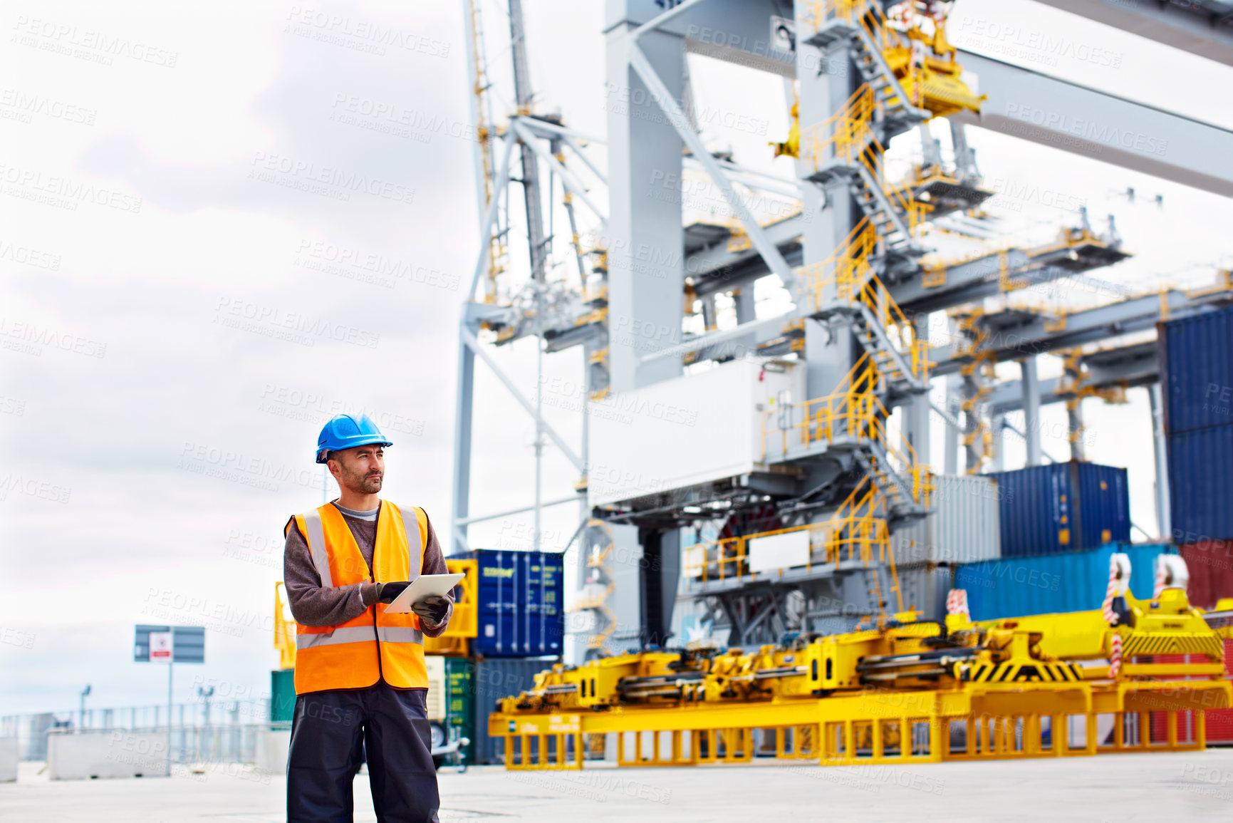 Buy stock photo Shot of a young man in workwear using a digital tablet while standing on a large commercial dock