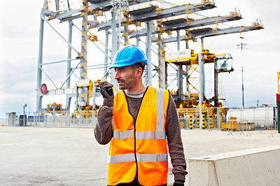 Buy stock photo Shot of a young man in workwear talking on a walkie talkie while standing on a large commercial dock