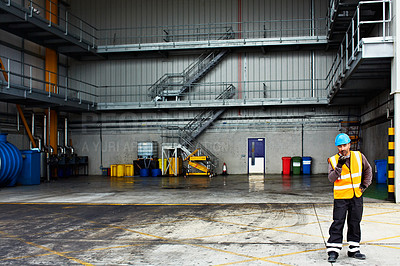 Buy stock photo Shot of a young man in workwear talking on a walkie talkie while standing on a large commercial dock