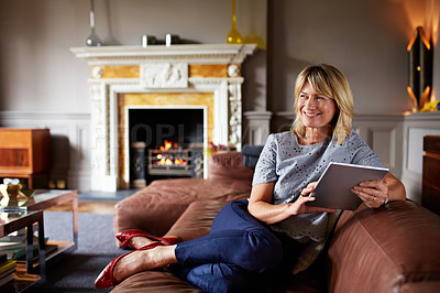 Buy stock photo Shot of a mature woman sitting on her sofa using a digital tablet