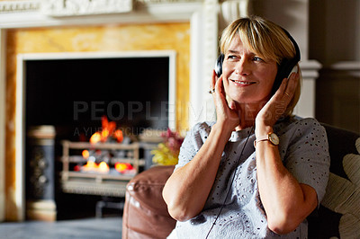 Buy stock photo Shot of a mature woman sitting on her sofa listening to music on headphones