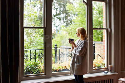 Buy stock photo Shot of a mature woman drinking tea while looking out of her living room window