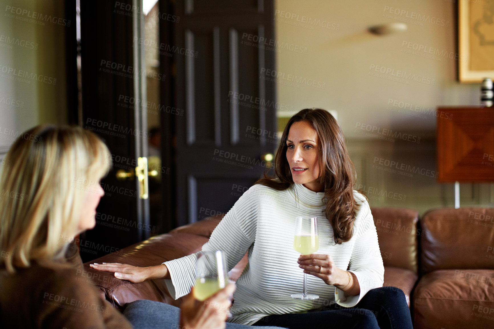 Buy stock photo Shot of two women sitting on a sofa drinking wine and talking