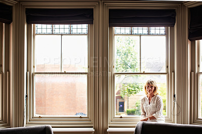 Buy stock photo Portrait of a smiling mature woman sitting by a window at home
