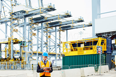 Buy stock photo Shot of a man in workwear standing outside on a large commercial dock using a digital tablet