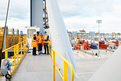 Buy stock photo Shot of three workers talking together while standing on an overhead walkway at a commercial dock