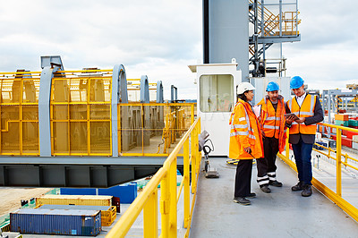 Buy stock photo Shot of three workers talking together while standing on an overhead walkway at a commercial dock