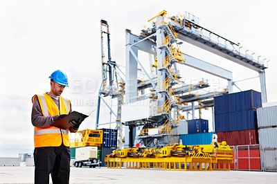 Buy stock photo Shot of a young man in workwear using a digital tablet while standing on a large commercial dock
