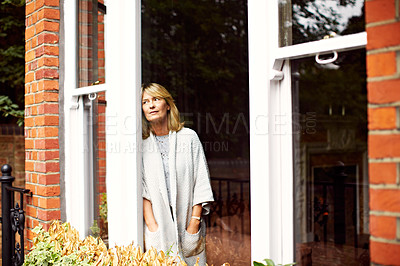Buy stock photo Shot of a mature woman looking out of her living room window