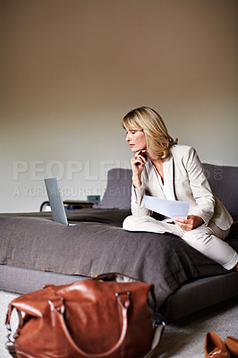 Buy stock photo Shot of a mature businesswoman going over some paperwork while sitting on her hotel bed