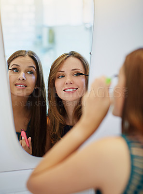 Buy stock photo Shot of two young friends putting on mascara in the bathroom mirror
