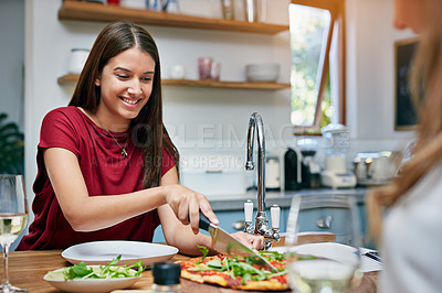 Buy stock photo Shot of two friends sitting at the kitchen table eating pizza and drinking wine