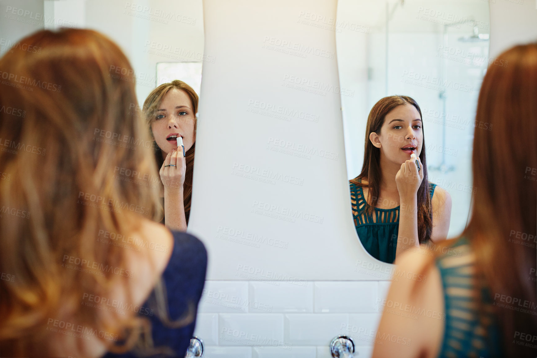 Buy stock photo Rearview shot of two young friends putting on makeup in the bathroom mirror