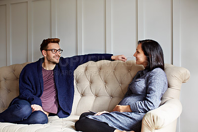 Buy stock photo Shot of a young pregnant woman talking with her husband on their sofa