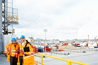 Buy stock photo Shot of three coworkers in protective workwear standing on a large commercial dock