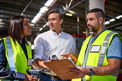 Buy stock photo Shot of three workers talking together over a clipboard inside of a warehouse