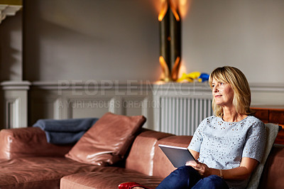 Buy stock photo Shot of a mature woman sitting on her sofa using a digital tablet