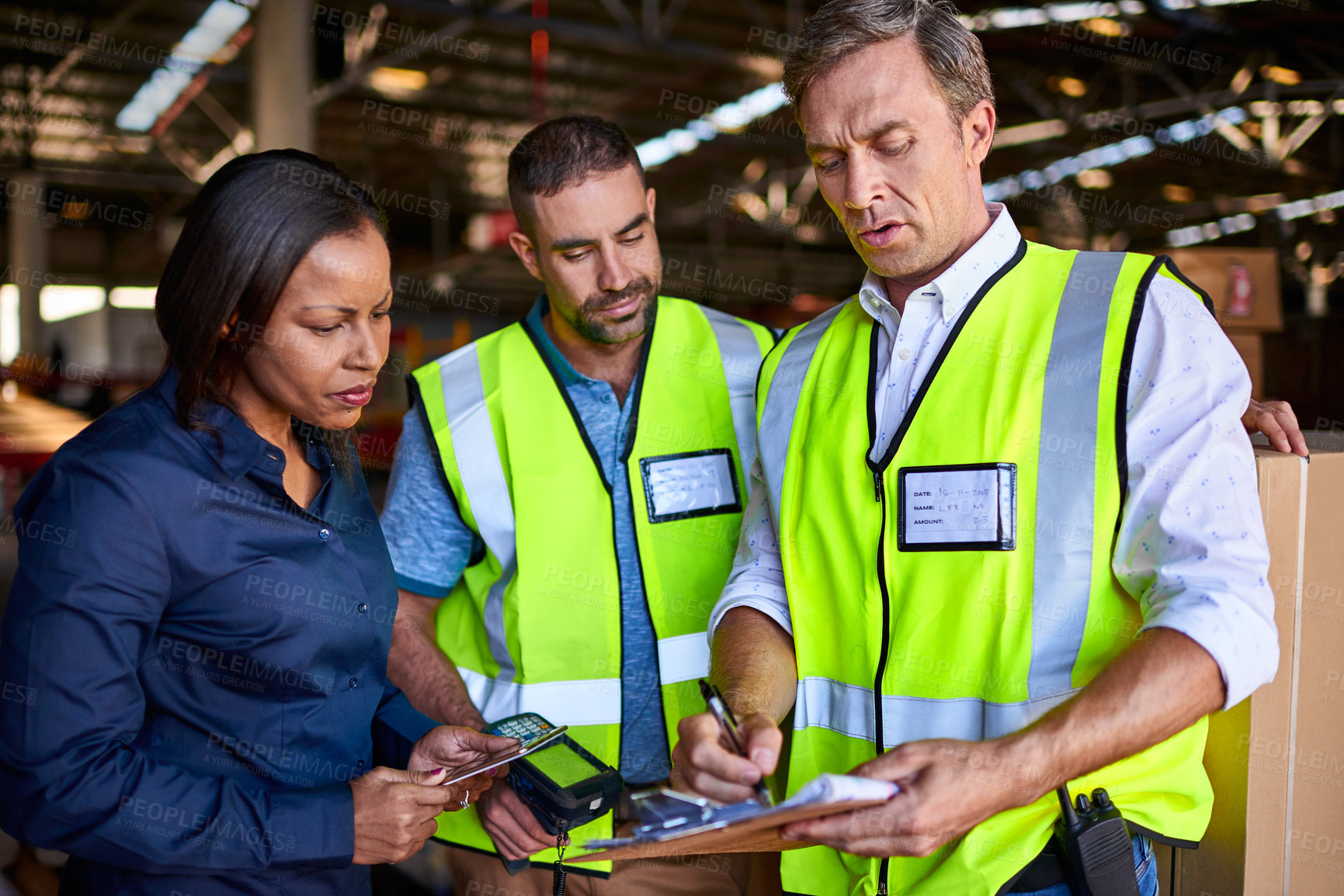 Buy stock photo Shot of three workers talking together over a clipboard inside of a warehouse