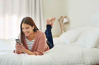 Buy stock photo Shot of a young woman lying on her bed using a cellphone