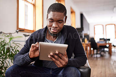 Buy stock photo Shot of a young man using a digital tablet while sitting in an office