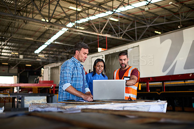 Buy stock photo Shot of a group of coworkers talking together over a laptop while standing in a large warehouse